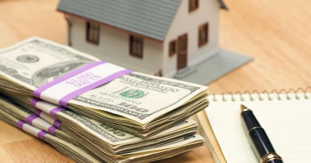 a stack of cash, house figurine and a notepad on a table