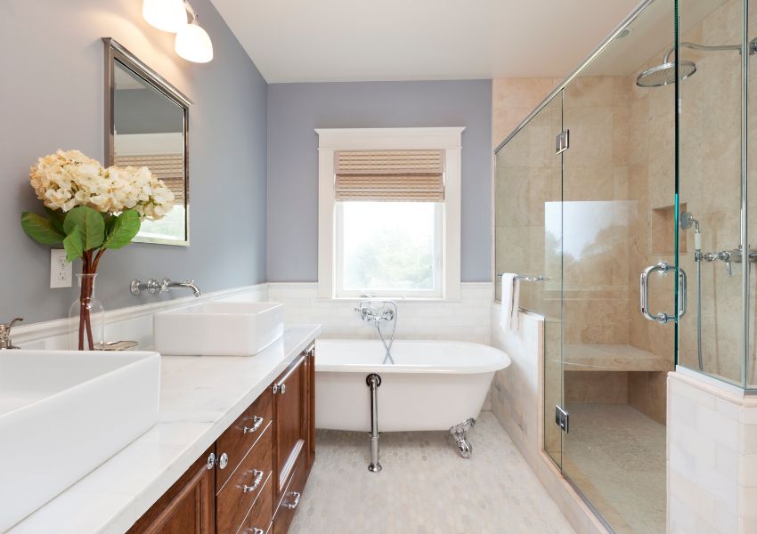 A neutral toned bathroom is pictured with two white sinks facing a mirror across from a glass shower, both of which are in front of a porcelain bathtub.