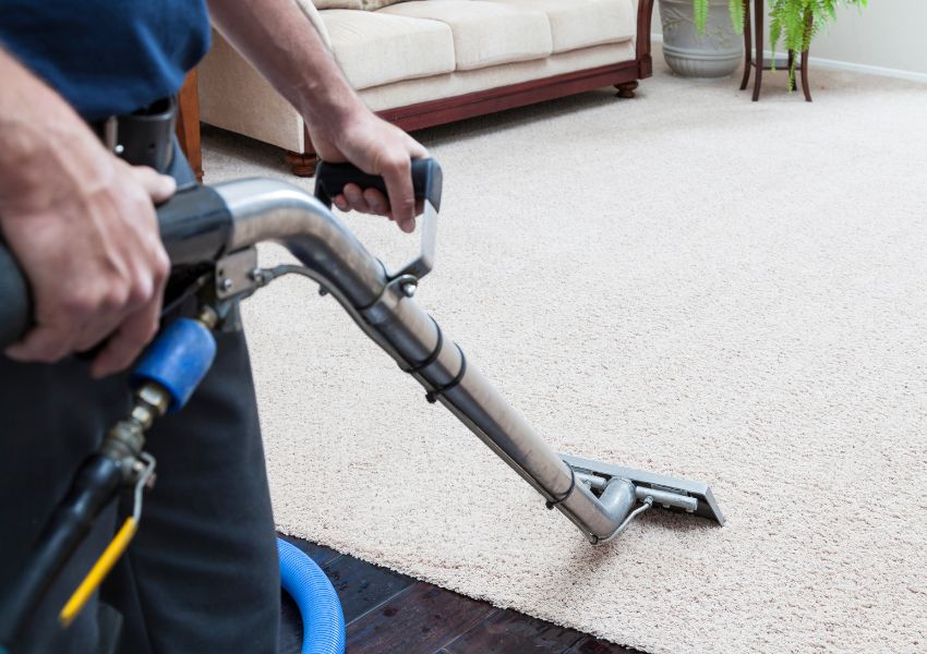 A property manager vacuums and steam cleans a cream rental property carpet after a tenant moves out.