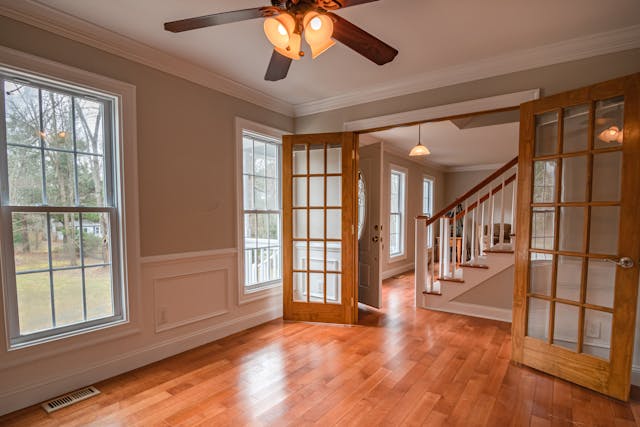 The interior of an empty room with a ceiling fan and clean wooden floors.