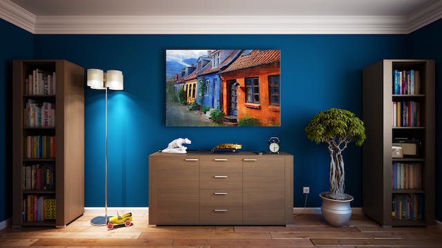 A bedroom wall with a dresser, bookshelves, and large painting.