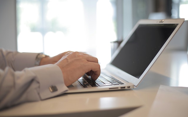 hands typing on a laptop with a window in the background