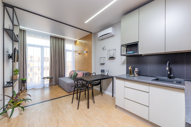 open-concept living room and kitchen with light wood floors, large windows, and white cabinets