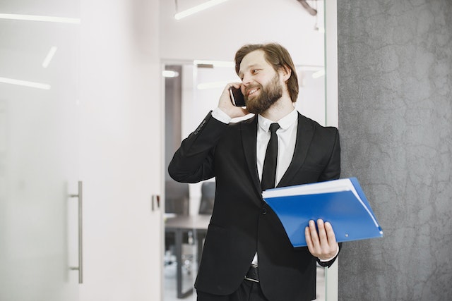 person in a black suit on the phone while holdings a blue folder